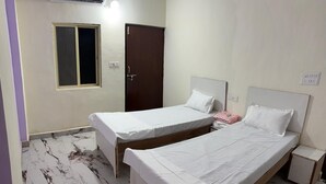 A room with two single beds, a window, an air conditioner, and a door. - BSSN Guest House (Gwalior)