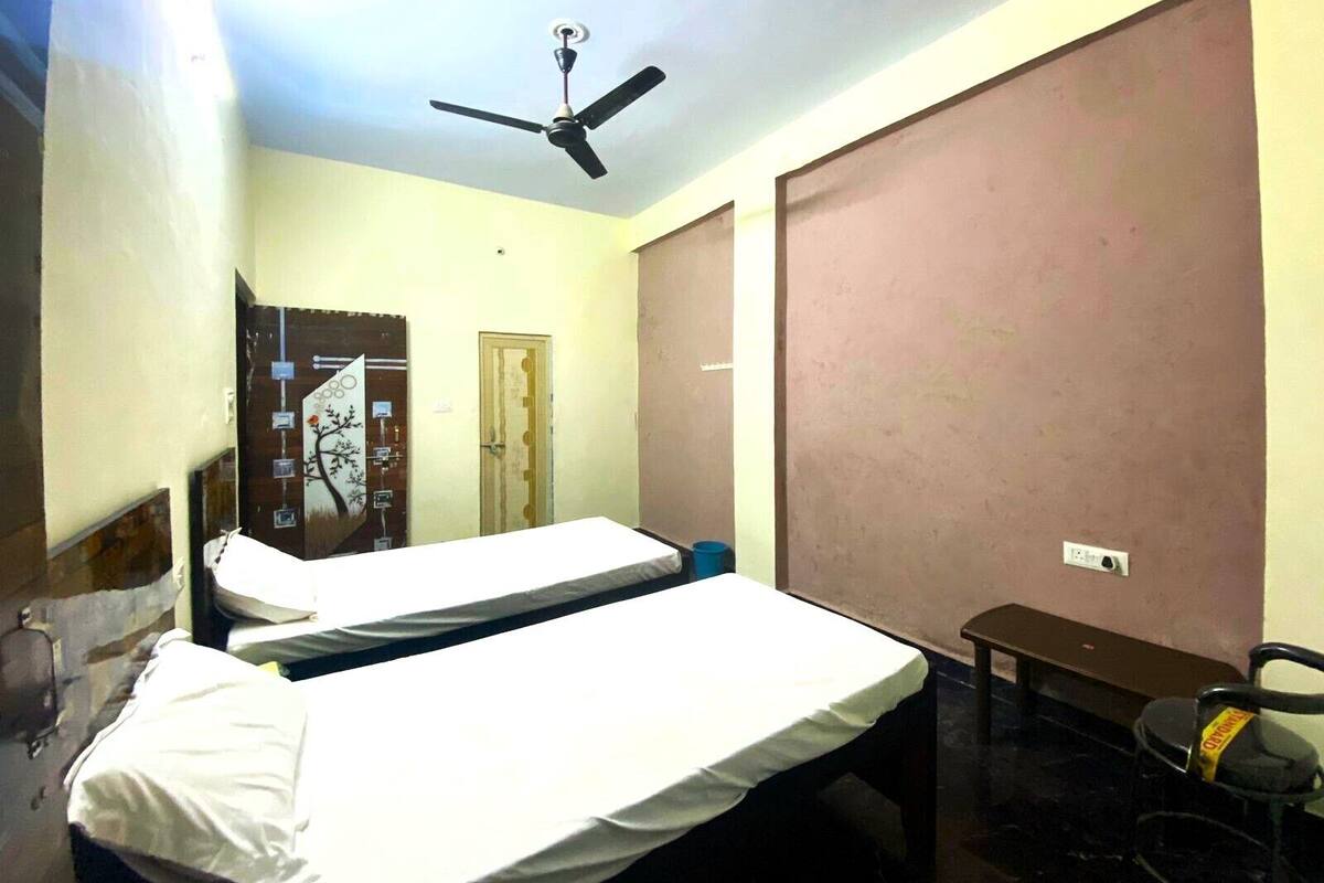 Une chambre avec deux lits simples, un ventilateur de plafond, une petite table et une chaise.