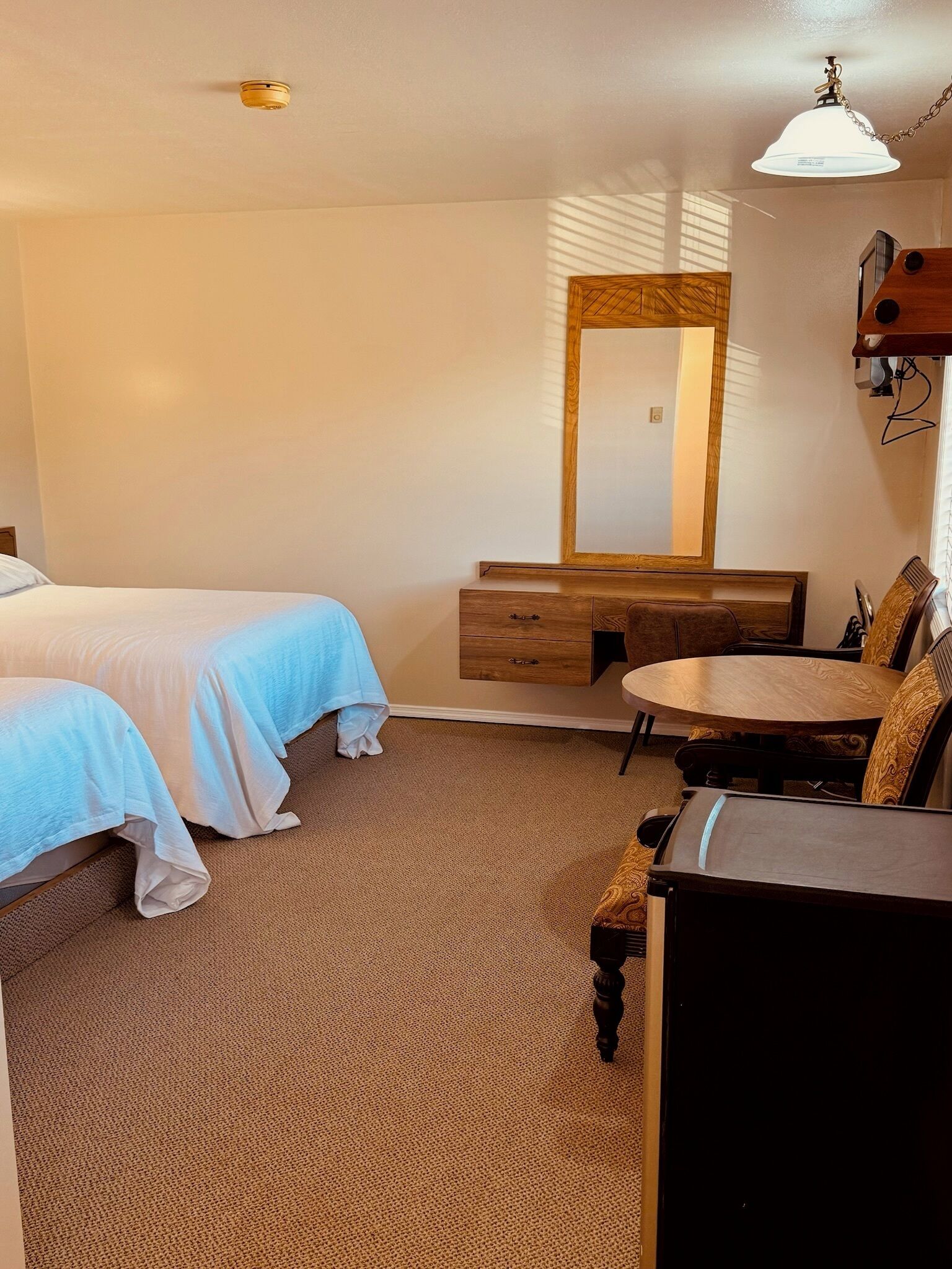 Une chambre d’hôtel avec deux lits, une commode en bois, une table ronde et un miroir.