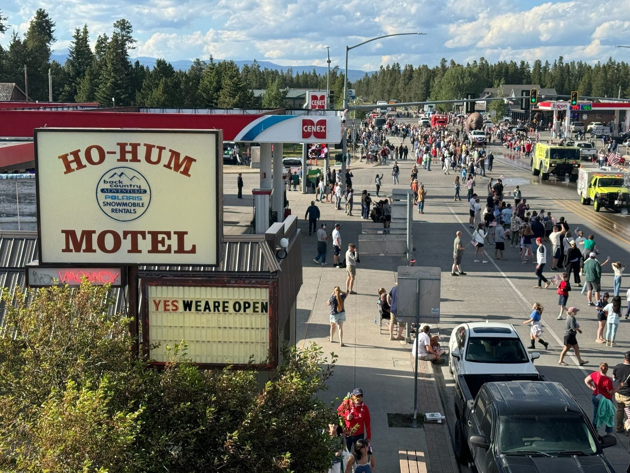 A busy street scene with a motel sign, a gas station, and a crowd of people.