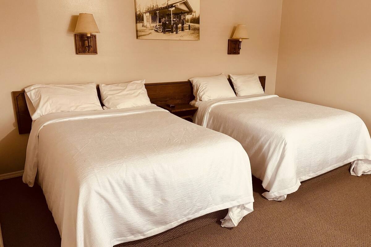 A hotel room with two beds, a wooden headboard, a wall-mounted lamp, and a vintage photo.