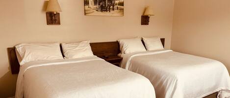 A hotel room with two beds, a wooden headboard, a wall-mounted lamp, and a vintage photo.
