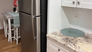 A kitchen with white cabinets, a stainless steel refrigerator, a granite countertop, and a small dining table with chairs.