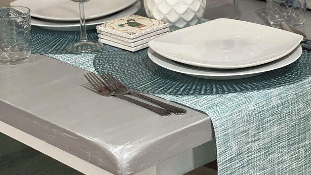 A dining table set with white plates, a clear glass, a wine glass, and a white vase with red flowers.