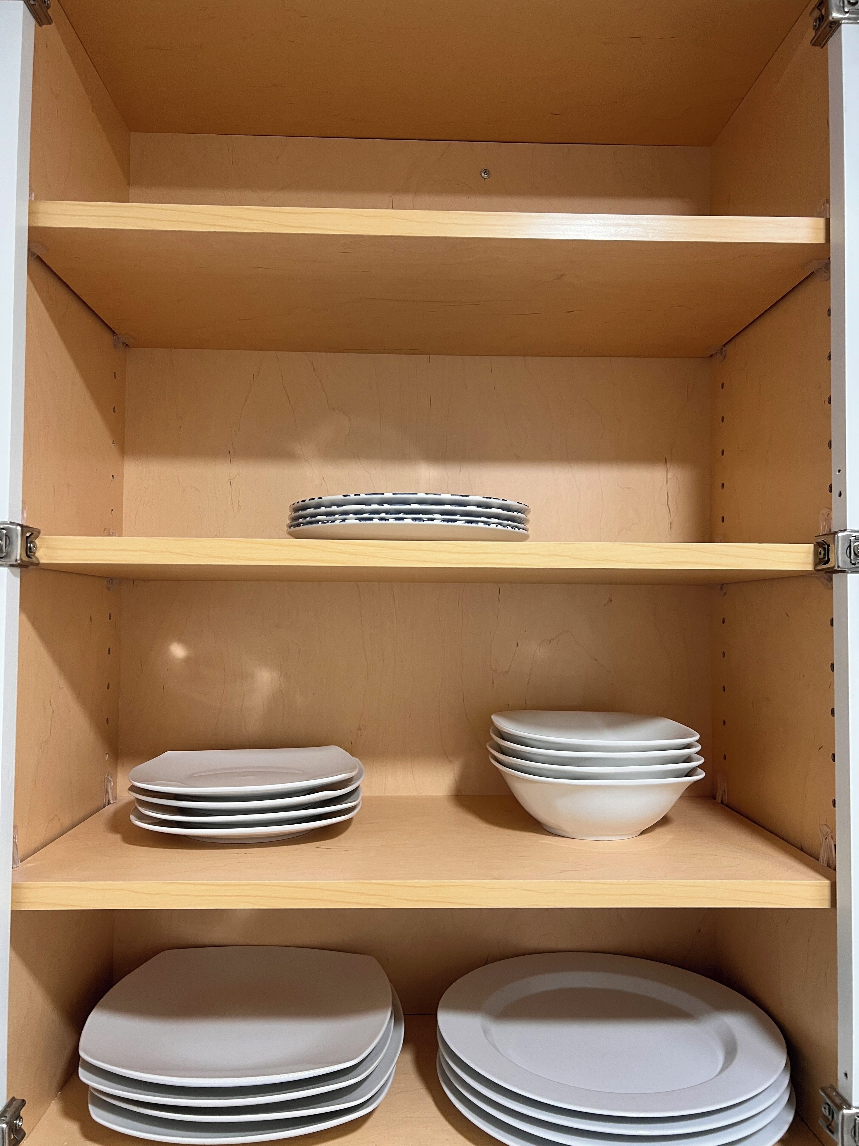 A wooden cabinet with three shelves, each holding stacks of plates and bowls.