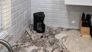 A kitchen with white subway tile backsplash, a coffee maker on the counter, and a knife block on the right.