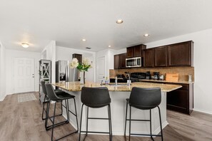 A modern kitchen with dark wood cabinets, a granite countertop, and a central island with bar stools. - Spacious 5 Bedroom-SeaWorld/Lackland Family Retreat (San Antonio)