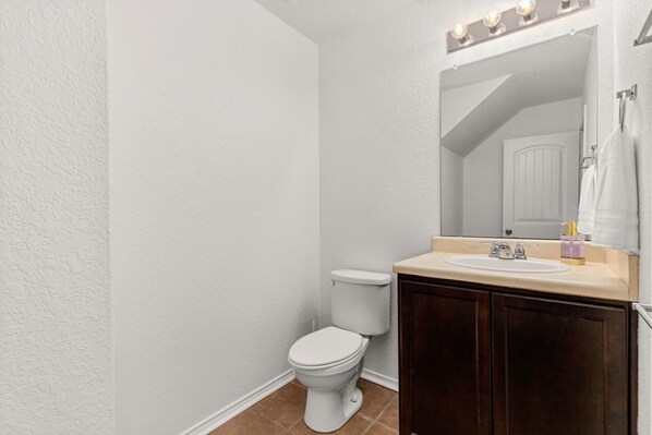 A bathroom with a white toilet, a sink with a vanity, and a mirror with lights. - Spacious 5 Bedroom-SeaWorld/Lackland Family Retreat (San Antonio)