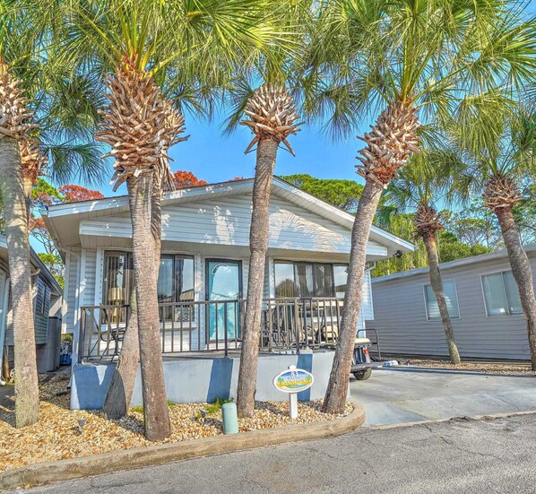 A single-story house with a porch, surrounded by palm trees.