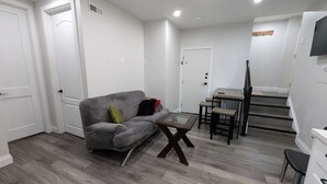 A modern living room with a grey sofa, a glass coffee table, and a dining area with a small table and chairs.