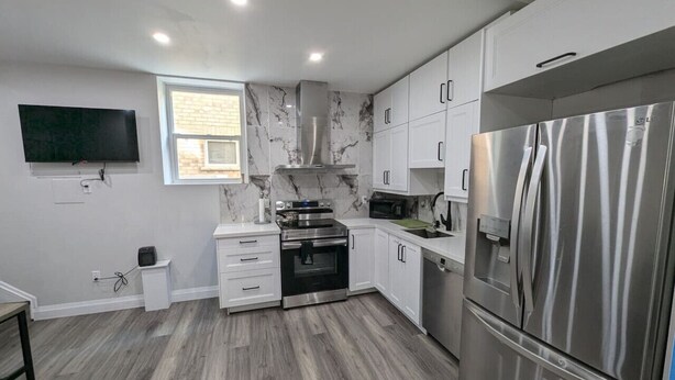A modern kitchen with white cabinets, a stainless steel refrigerator, and a built-in oven.