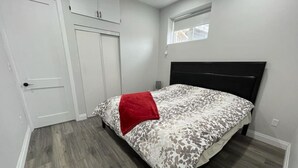 A bedroom with a bed, a red throw, a window, and a door.