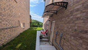 A narrow brick corridor with a concrete pathway, a red chair, and a potted plant.