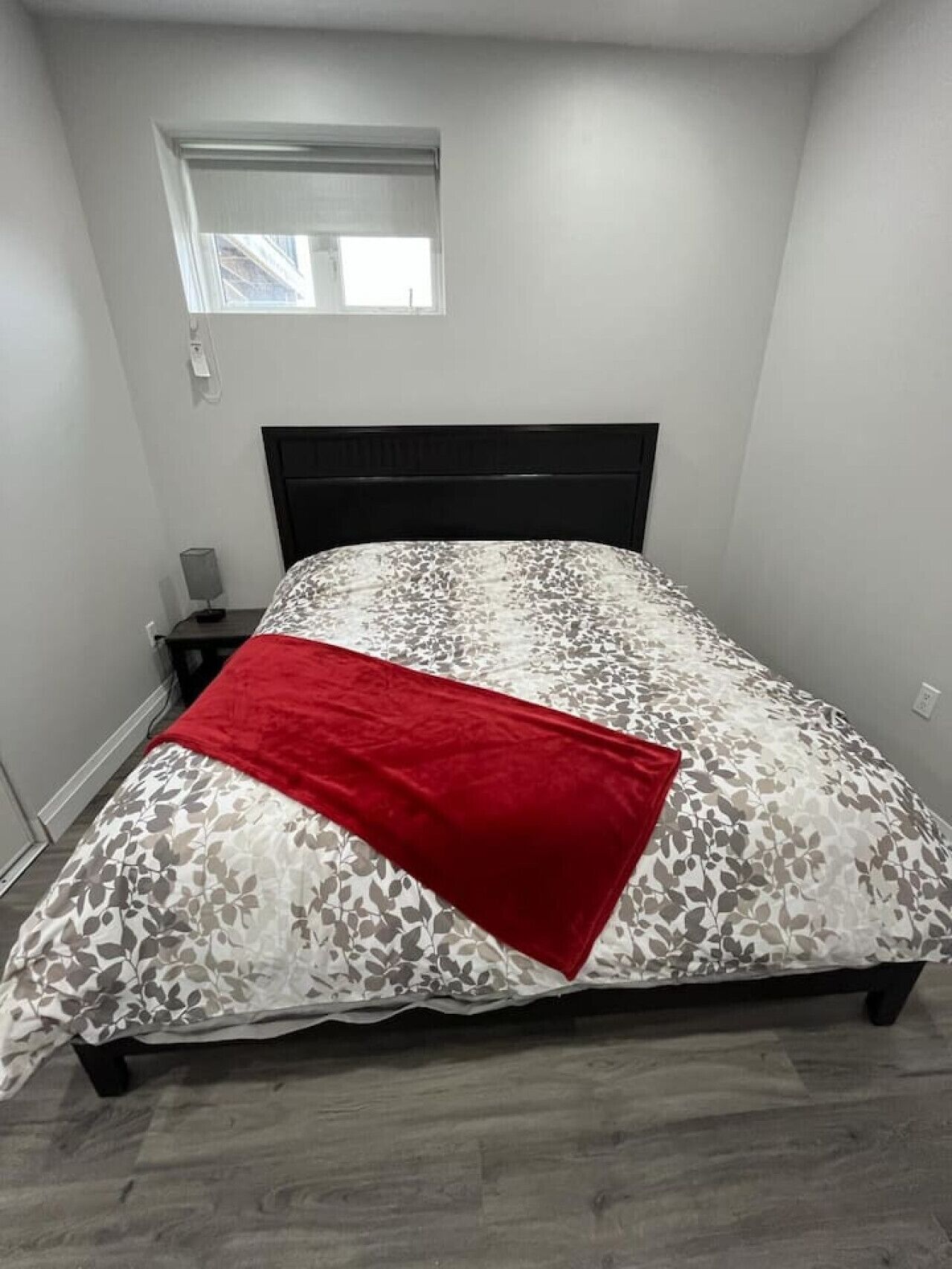 A bedroom with a bed, a nightstand, a lamp, and a window.