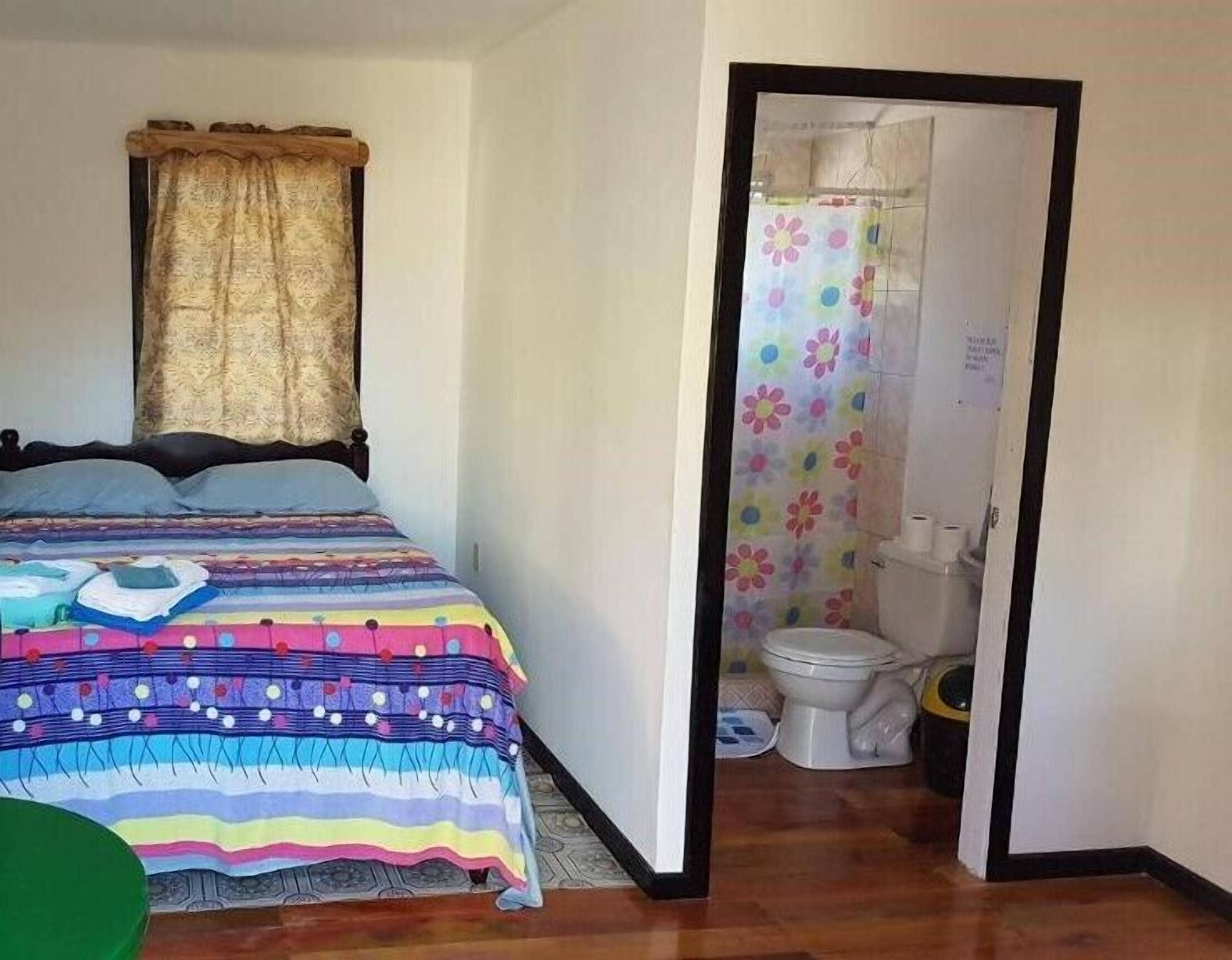 Camera da letto con un letto, una finestra con tende e bagno con il water e tenda per la doccia.