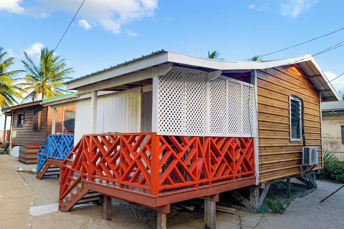 Una casa de madera con un balcón de celosía roja, una puerta blanca y una ventana con una manguera negra.