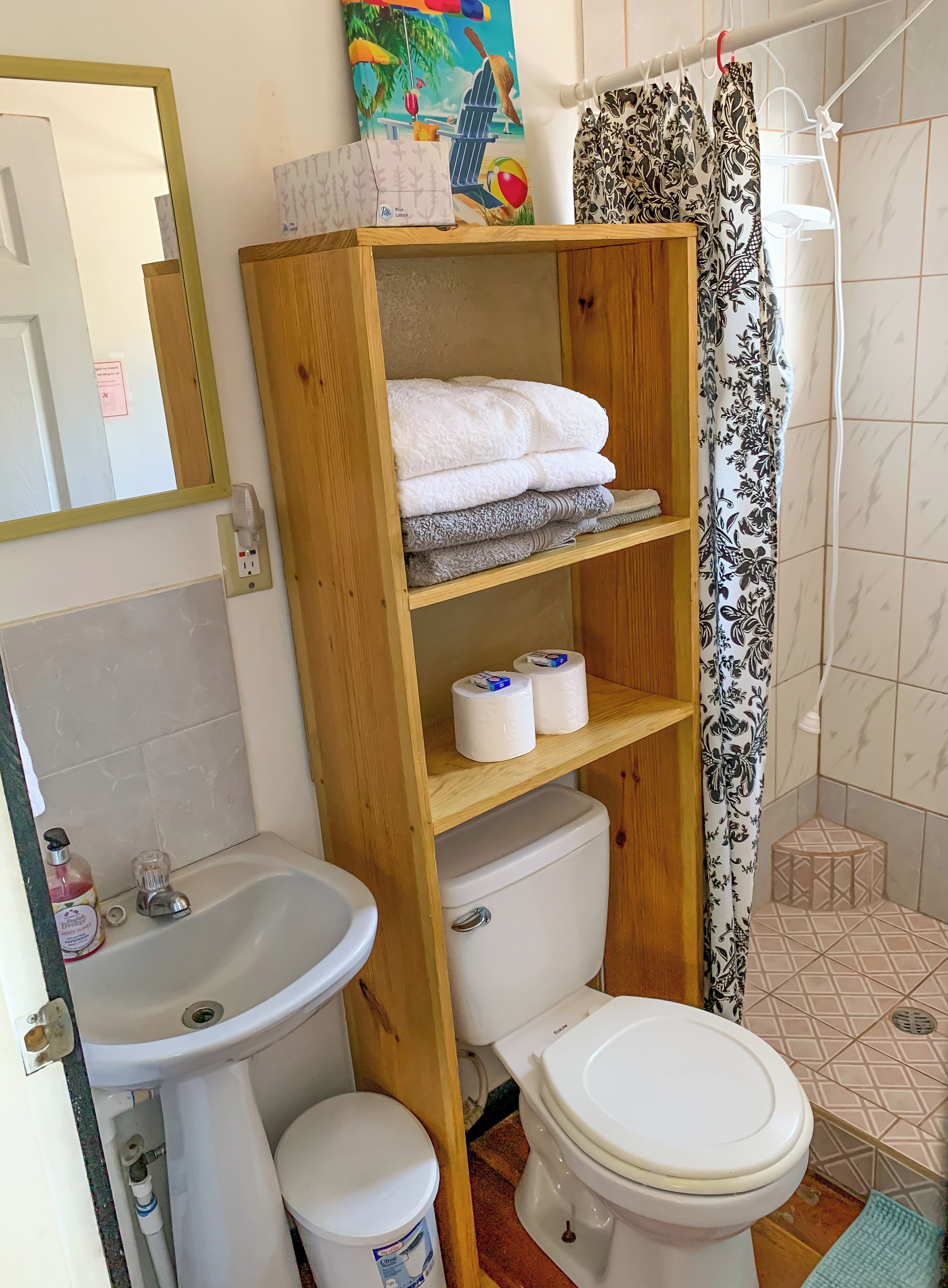 Kylpyhuoneessa on puinen hylly, jossa on pyyhkeitä, wc-istuin, pesuallas ja suihkuverho.
