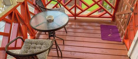 A wooden deck with a table and two chairs, a purple mat, and a red railing.