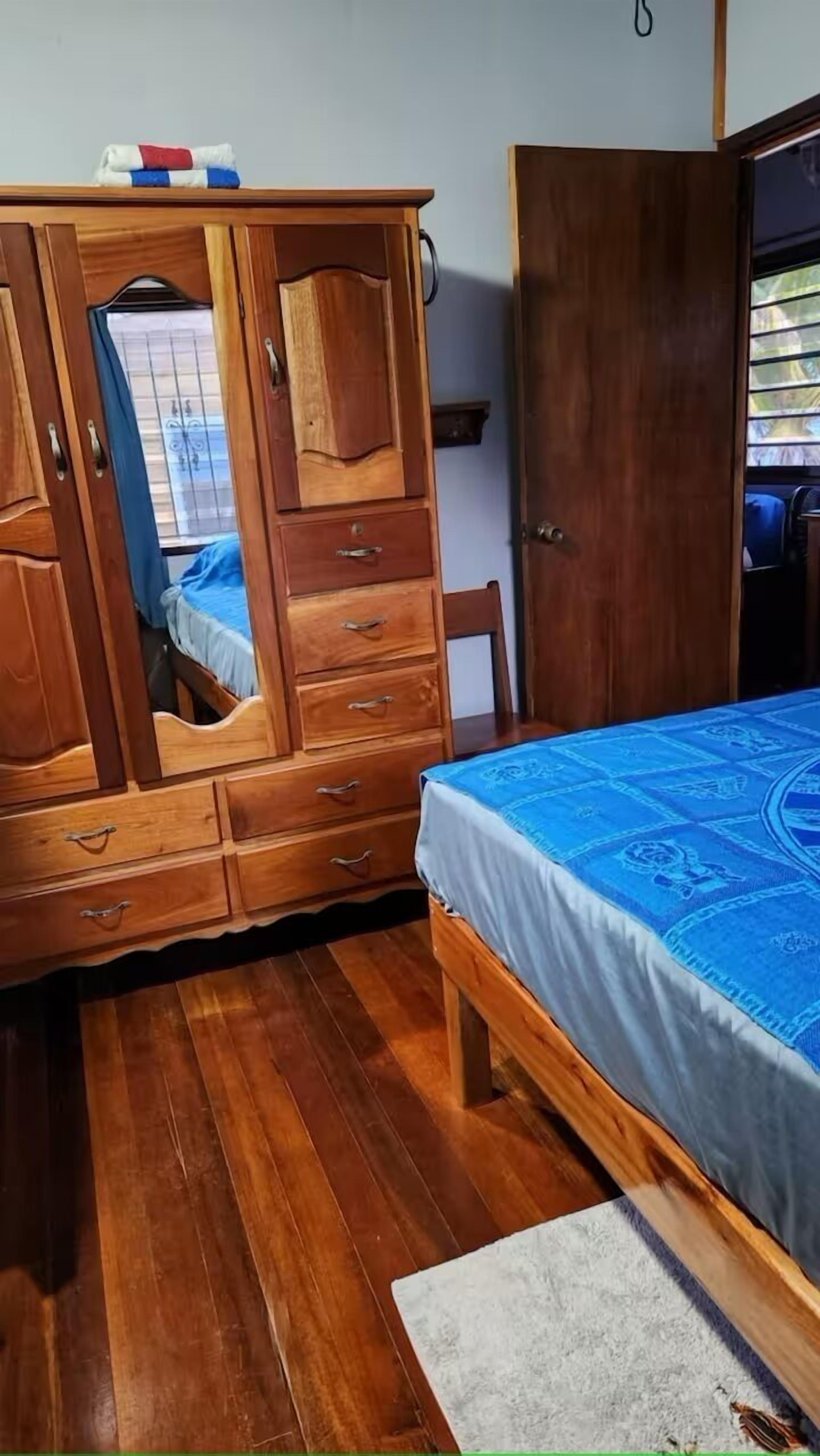 Une chambre avec une armoire en bois, un lit recouvert d’une couvre-lit à motifs bleus et un plancher en bois.