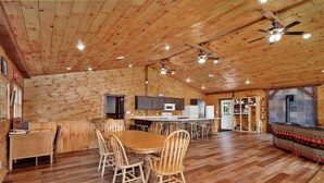 A spacious wooden cabin with a large dining table, multiple chairs, a kitchen area, and a fireplace.