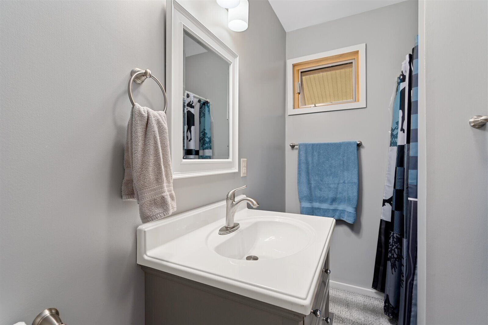 A bathroom with a white sink, a mirror, and two towels hanging on towel bars.
