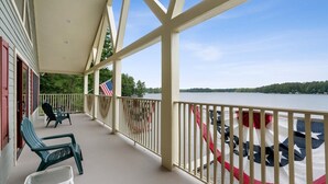 A covered porch with chairs and a flag, overlooking a lake.