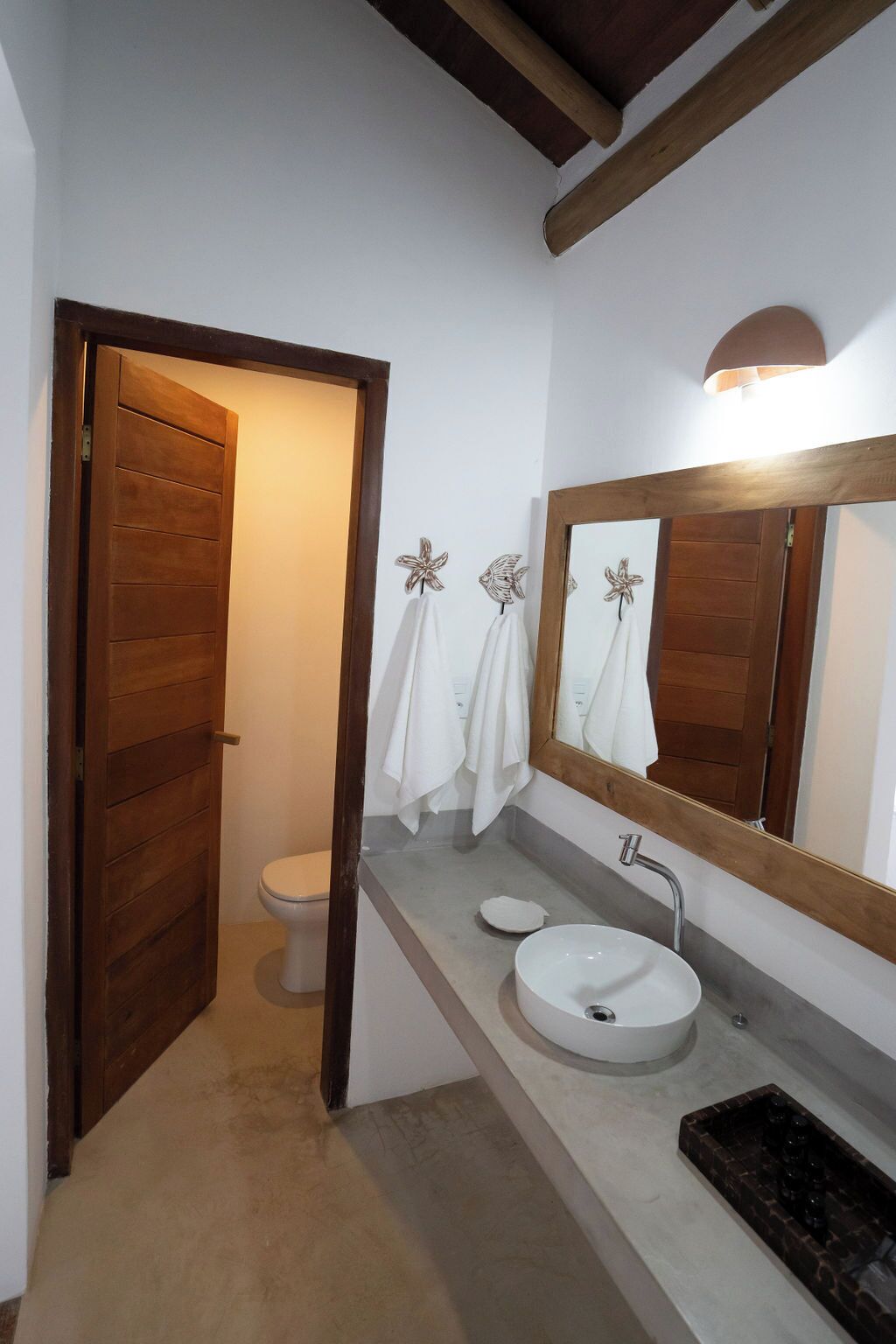 A bathroom with a wooden door, a toilet, a sink with a mirror, and a towel rack with towels.