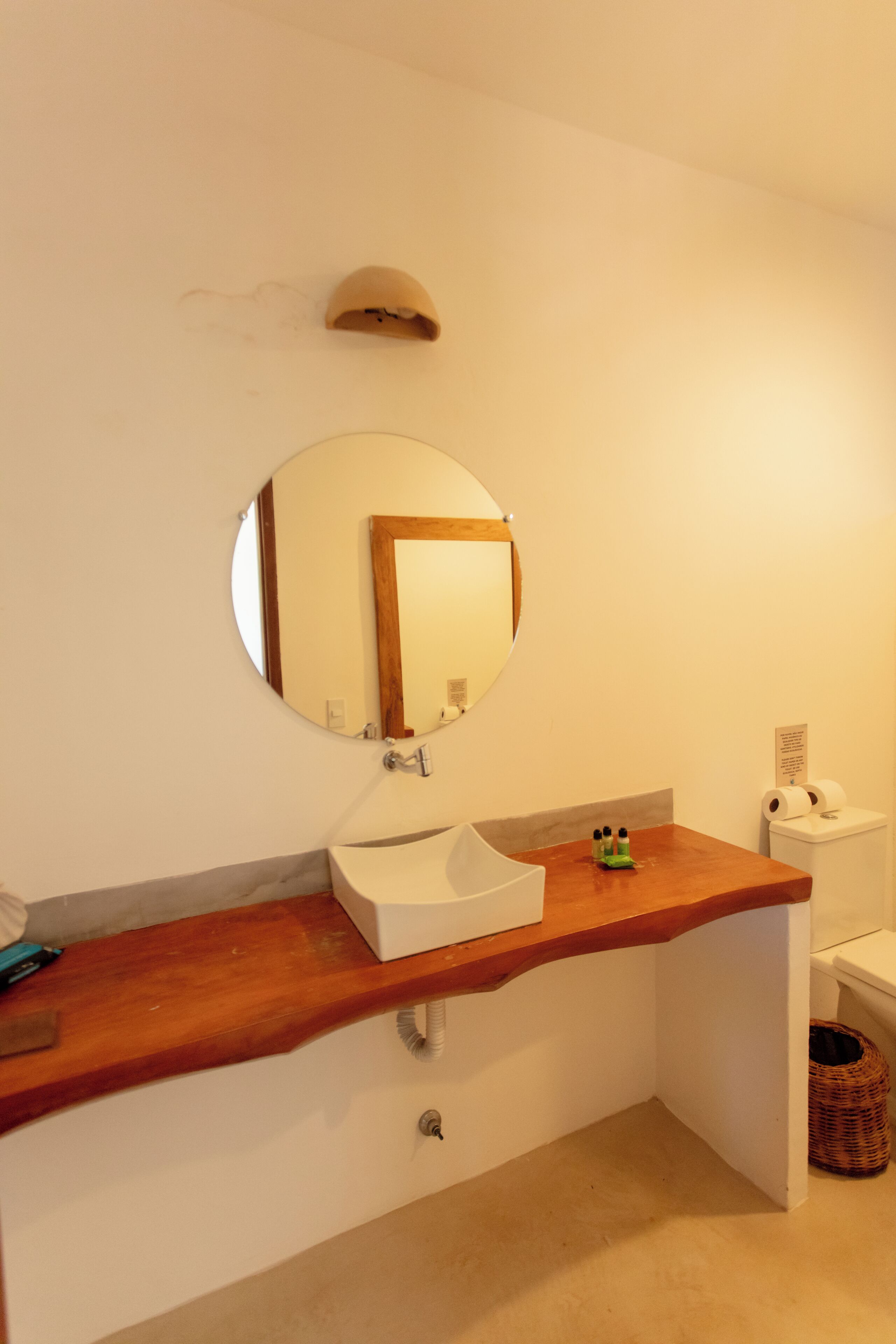 A bathroom with a wooden vanity, a round mirror, a white sink, and a toilet.