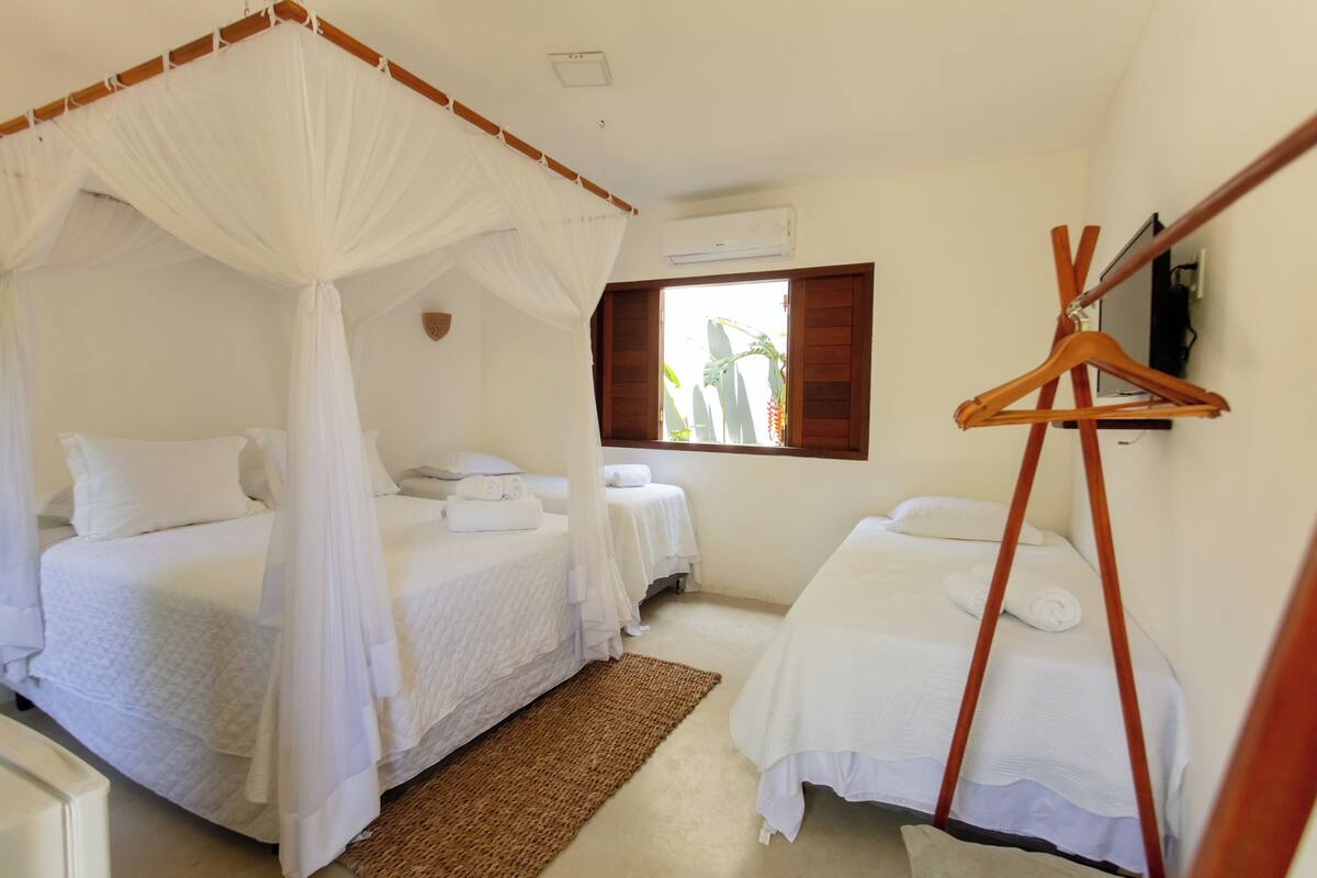 A room with two beds, a wooden hanger, and a window with a view of greenery.