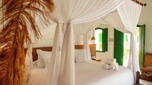 Una habitación con una cama bajo un dosel, un banco de madera y un tapete tejido.