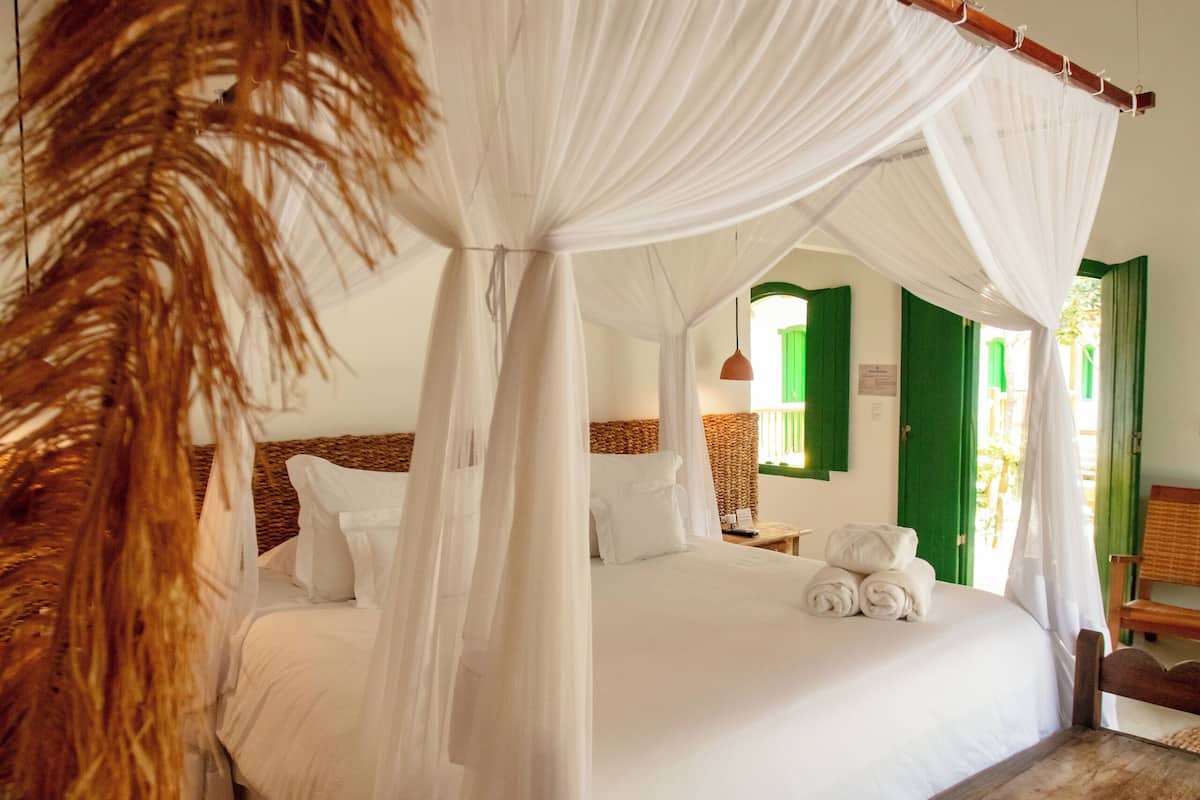 A room with a bed under a canopy, a wooden bench, and a woven rug.