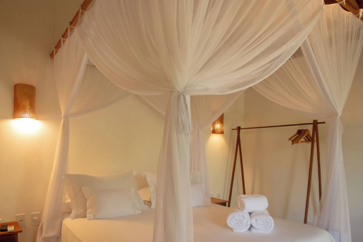 A four-poster canopy bed with white linens and a rolled towel on the bed.