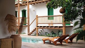 Una terraza de madera con piscina, sillas de descanso y una escalera que lleva a un balcón.
