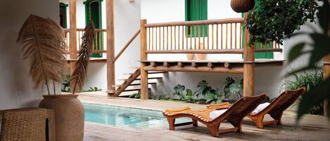 A wooden deck with a pool, lounge chairs, and a staircase leading to a balcony.