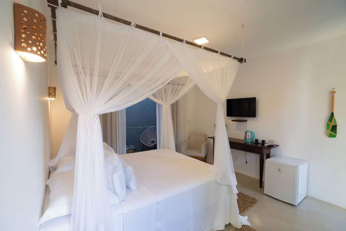 A bedroom with a canopy bed, a television, a desk, and a minibar.