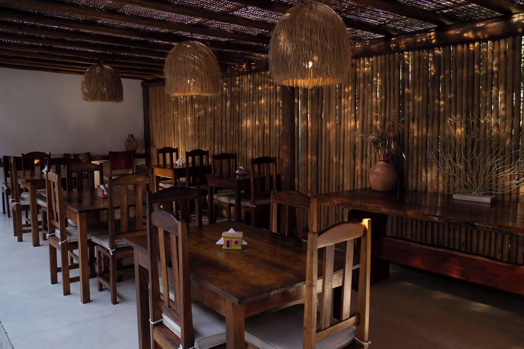 Un restaurante con mesas y sillas de madera, lámparas colgantes y una pared de bambú.