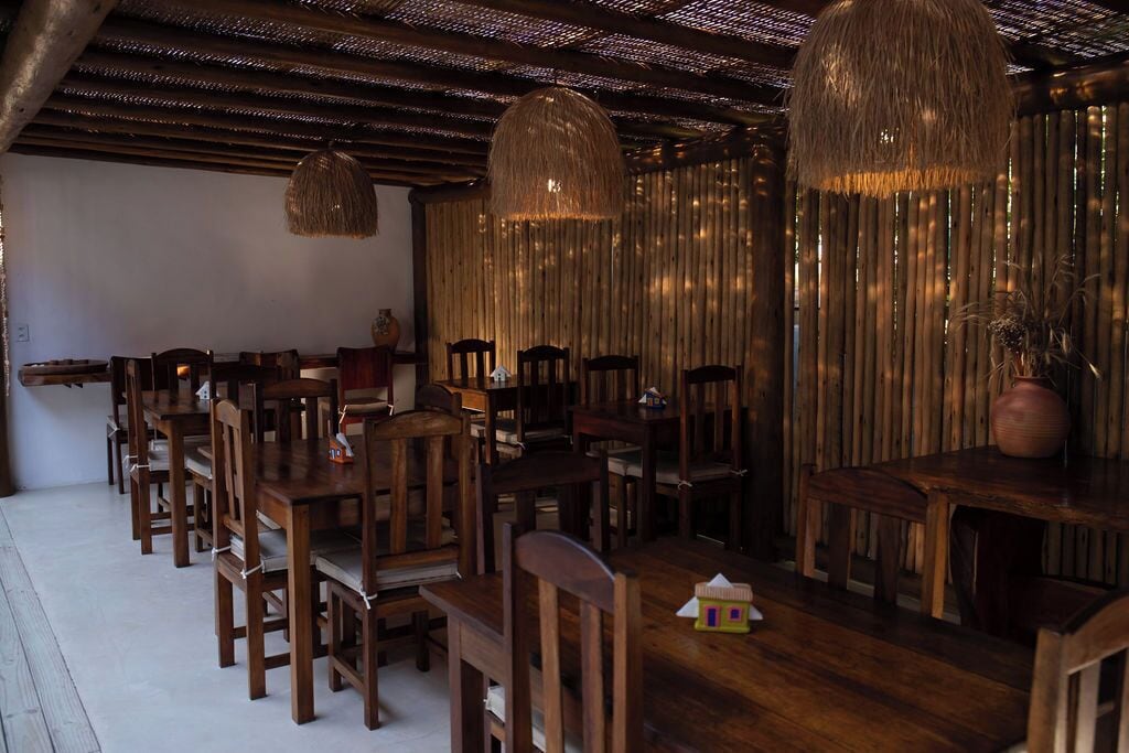 A dining area with wooden tables and chairs, hanging light fixtures, and a rustic wooden wall.