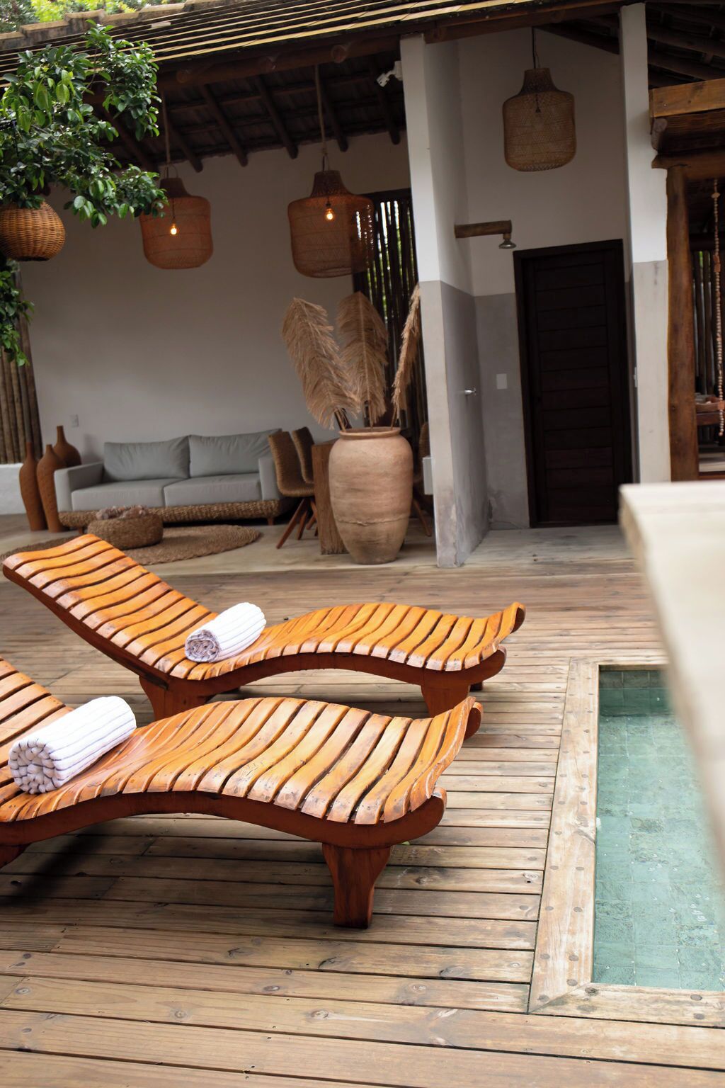 Eine Holzterrasse mit zwei Liegestühlen, einem Sofa und einer großen Vase mit getrockneten Pflanzen.