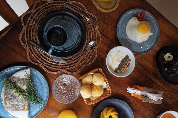 A breakfast setting with plates of food, a cup, and a basket of bread. - Corais de Trancoso Pousada (Porto Seguro)