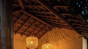 Un espacio interior acogedor con techo de madera, luminarias tejidas, un sofá, una mesa de comedor con sillas, un televisor de pantalla plana y un jarrón grande.