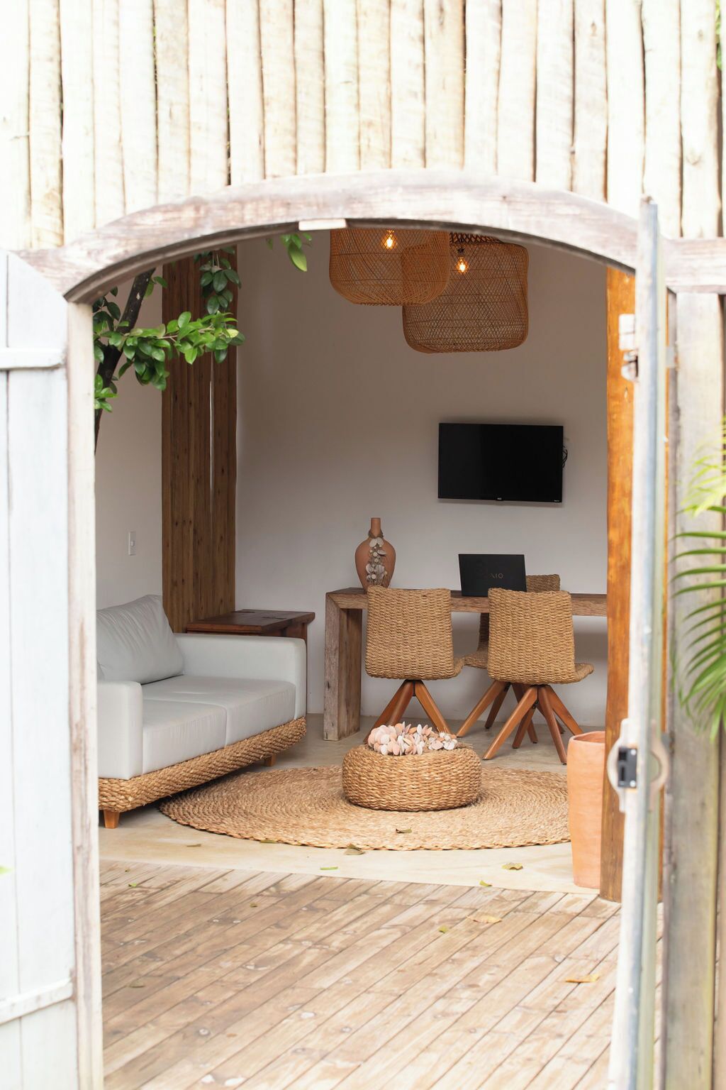 Een gezellige zithoek met een witte bank, rieten stoelen, een kleine tafel en een flatscreen televisie aan de muur.