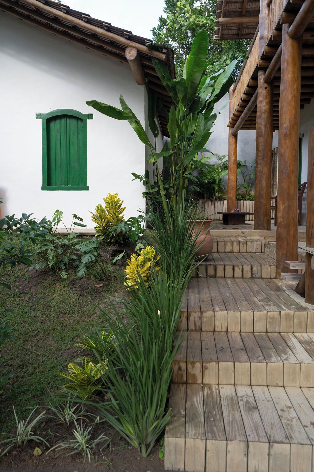 A wooden staircase leading to a porch with a white wall and green shutters.