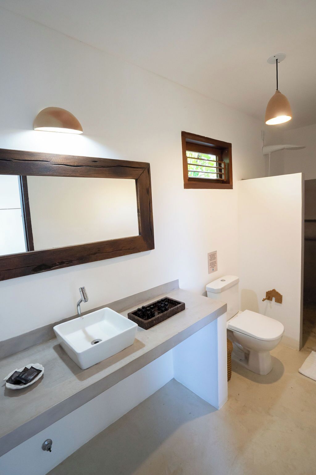 Une salle de bain moderne avec un grand miroir, un lavabo blanc et une petite fenêtre.