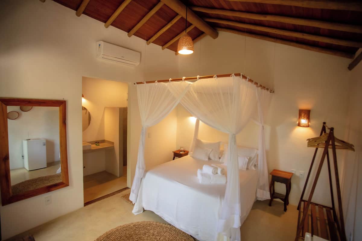 A bedroom with a four-poster bed, a bedside table, a mirror, and a small wooden stool.