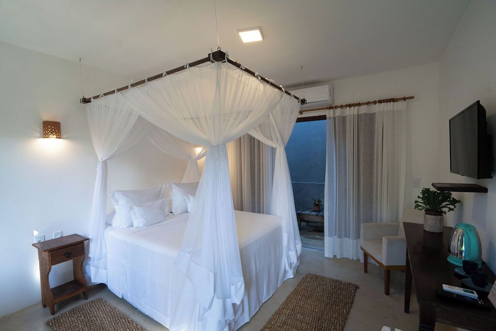 A bedroom with a four-poster bed, a desk with a plant, and a TV on the wall.