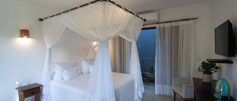 A bedroom with a four-poster bed, a desk with a plant, and a TV on the wall.