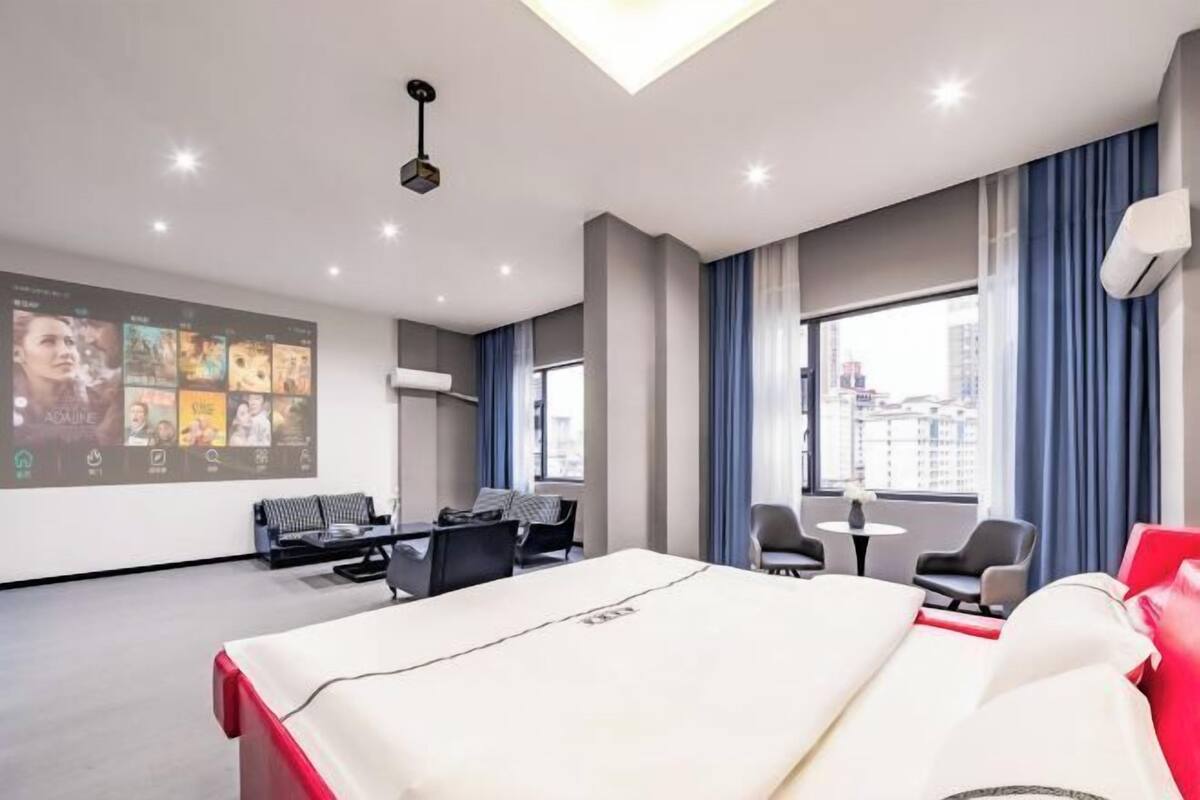 Ein modernes Hotelzimmer mit Bett, Sitzecke und einem großen Bildschirm, der Bilder zeigt.