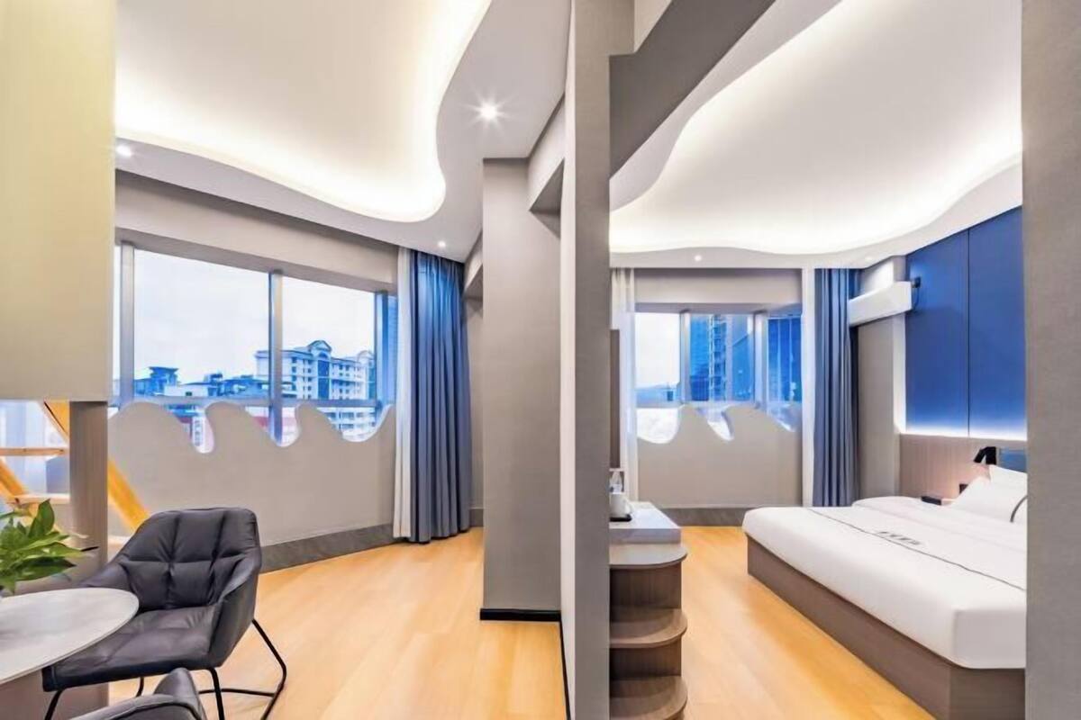 Ein modernes Hotelzimmer mit gewölbter Decke, einem Bett, einer Sitzecke und großen Fenstern mit Blick auf die Stadt.