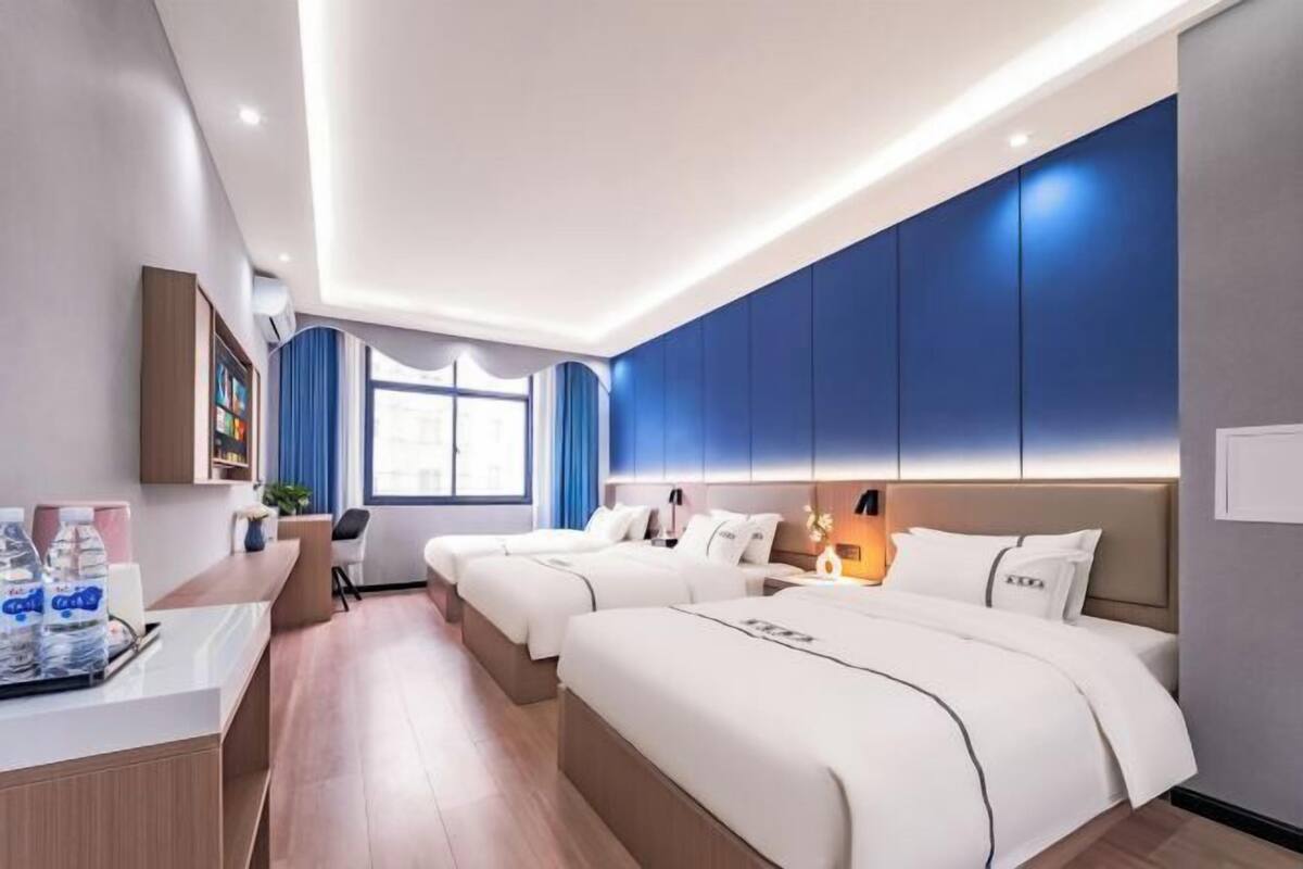 Ein Hotelzimmer mit zwei Betten, einem Schreibtisch mit Wasserflaschen und einem Fenster mit Vorhängen.