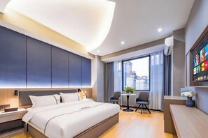 A modern hotel room with a large bed, a desk, a chair, and a view of the city.